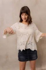 Blusa de punto calado color blanco, con diseño geométrico y floral transparente, escote redondo y mangas tres cuartos amplias de calce relajado.