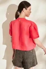 Blusa de lino color amarillo, con cuello mao, cierre frontal con cremallera y mangas cortas abullonadas. Cuenta con un bolsillo aplicado en el frente.