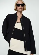 Chaqueta tipo bomber color negro, con diseño oversize, cuello redondo, cierre frontal de cremallera y dos bolsillos laterales con solapa.