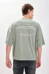 Camiseta verde de corte amplio y recto, con estampado de texto circular en la espalda.