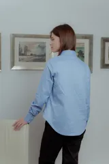 Camisa celeste de poplin de algodón, corte irregular con tablas al frente, cuello clásico y mangas largas.