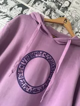 Canguro lila con capucha y cordones, con estampado circular en el frente con símbolos y letras. Diseño inspirado en el personaje Maga Oscura del anime Yu-Gi-Oh!.