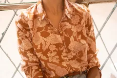 Camisa de corte clásico con cuello camisero y cierre frontal de botones, manga larga con puños abotonados, confeccionada en tela con estampado floreado en tonos camel y rosa.