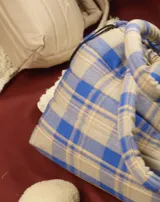 Bolso tipo tote bag de franela a cuadros en tonos azul y beige, con asas tubulares acolchadas y cierre con cordón ajustable.