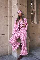 Conjunto de dos piezas de pijama confeccionado en algodón a cuadros vichy rosados y blancos. Incluye una camisa de manga larga con puños acampanados y cierre delantero con cordones para atar, y un pantalón largo de corte recto con volados en el ruedo.