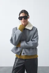 Campera corta de paño color gris con cuello de corderito blanco, cierre frontal con botones y bolsillos laterales.