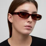 Lentes de sol con montura ovalada y ligeramente plana, estilo ojo de gato, en color carey (marrón jaspeado). Los lentes son polarizados de color marrón.