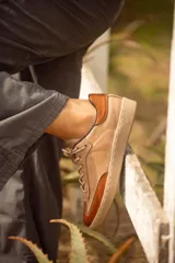 Zapatillas urbanas de cuero color taupe con detalles en terracota, cordones al tono y suela marrón.