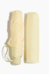 Paraguas plegable de color amarillo pálido o crema, con funda a juego. Se muestra cerrado y enrollado, con una correa de tela en el mango.