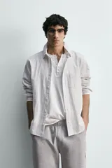 Camisa de corte relajado confeccionada en tejido de algodón con textura, diseño a rayas verticales, cuello abotonado, manga larga con puños y bolsillo de plastrón en el pecho.