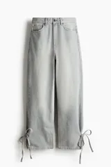 Jean barrel de tiro alto confeccionado en denim de algodón rígido color gris claro con efecto deslavado, diseño curvo en las piernas y tiras finas para anudar en los bajos.