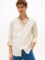 Camisa de manga larga color beige claro, corte slim fit, con cuello abotonado, cierre con botones y logo de Tommy Hilfiger bordado en el pecho.