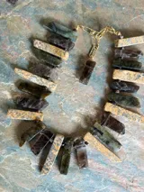Collar artesanal confeccionado con piedras naturales en tonos tierra, gris y verdosos, con cierre y cadena de extensión dorados.