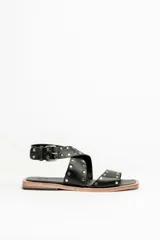 Sandalias bajas de cuero negro con tachas plateadas, tiras cruzadas y hebilla al tobillo.