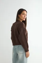 Cardigan de punto color marrón chocolate, con cuello redondo, cierre frontal de botones y diseño de costuras verticales visibles. Presenta puños y ruedo acanalados.