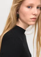 Jersey de punto fino acanalado en color negro, con cuello redondo y manga larga. Presenta un diseño entallado con bajo asimétrico y detalle de botones laterales decorativos.