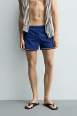 Short de baño azul con cintura elástica ajustable con cordón, bolsillos laterales y ribetes en contraste en los bordes.