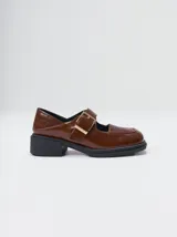 Zapatos tipo guillermina con punta cuadrada, confeccionados en lona resistente con estampado de cuadros escoceses en tonos beige, rojo y negro. Presentan una correa ajustable con hebilla metálica color bronce y una suela con taco de 4 cm.