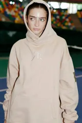 Buzo oversize color nude confeccionado en frisa, con capucha amplia, bolsillo canguro, terminaciones de puño y ruedo con rib, y logo de la marca bordado en el centro delantero.