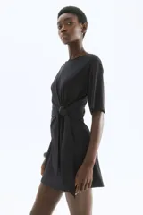 Vestido corto negro de punto con cuello redondo, mangas cortas y detalle de nudo en un lateral.