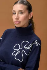 Sweater de punto color azul marino con cuello alto y diseño holgado. Presenta mangas con hombros caídos, terminaciones acanaladas y apliques de líneas orgánicas en relieve de color blanco que forman figuras florales en el frente y las mangas.