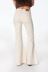 Pantalón de jean azul oscuro, corte acampanado (flare) de tiro alto, con costuras visibles en contraste y bordados tonales en la parte inferior de las piernas. El ruedo es deshilachado.