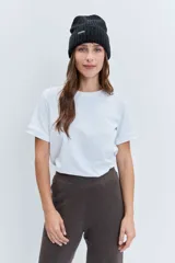 Gorro tipo beanie de punto grueso color amarillo pastel, con vuelta en el borde y etiqueta pequeña con logo en el frente.