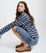 Bermuda tipo jorts de jean azul con lavado medio, corte holgado y largo por debajo de la rodilla. Presenta cintura con trabillas, bolsillos laterales y traseros, y cierre frontal con botón y cremallera.