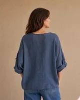 Blusa color azul jean con escote en V, cierre frontal con botones de madera y cordones ajustables, mangas largas con presilla y bolsillos delanteros con detalles desflecar.