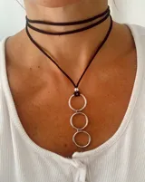 Gargantilla tipo choker confeccionada en cordón de símil gamuza negro, con dije colgante compuesto por tres argollas metálicas plateadas entrelazadas.