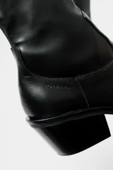 Bota de caña media estilo western, confeccionada en cuero negro, con taco cuadrado y punta cuadrada.