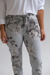 Pantalón de corte recto con cintura elástica y cordón ajustable, confeccionado en tela con estampado floral en tonos grises y blancos sobre base celeste.
