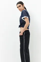 Pantalón de jean ancho color negro, de tiro bajo y confeccionado en algodón. Cuenta con una línea bordada color marrón en ambas piernas y cinco bolsillos.