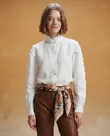 Camisa blanca de lino con cuello alto y volados, cierre frontal de botones y mangas largas con frunces en los hombros.