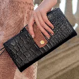 Billetera negra con textura símil piel de cocodrilo y cierre con broche a presión. Tiene un bolsillo externo con cierre y múltiples compartimentos internos para tarjetas y billetes.