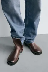 Bota de caña media fabricada en piel color marrón oscuro, con cierre de cremallera lateral, horma cuadrada y suela con ligero tacón.