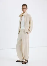 Chaqueta oversize color beige con cuello alto, cierre frontal de cremallera, bolsillos frontales con solapa y mangas largas.