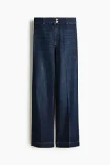 Jean de denim azul oscuro, de tiro alto y piernas amplias con pliegues frontales y traseros. Cuenta con cierre y doble botón metálico en la cintura.