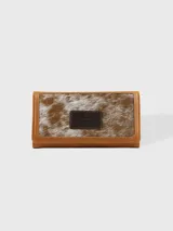 Billetera de cuero combinada en tonos camel y marrón, de formato rectangular con solapa. Cuenta con un parche central decorativo con logo grabado y detalles de costura perimetral.