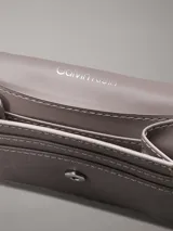 Billetera Calvin Klein de plegado triple, color gris con monograma de la marca en toda la superficie y barra plateada con el logo grabado.