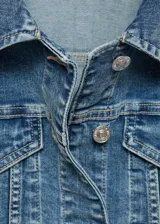 Chaqueta vaquera de corte ajustado y diseño corto, confeccionada en tejido de algodón estilo denim. Cuenta con cuello camisero de solapa, cierre frontal de botones metálicos, bolsillos de parche con solapa en el pecho y manga larga con puños abotonados.