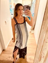 Vestido largo tejido en lurex color beige con diseño vertical y terminación en flecos negros. Breteles finos de cuero intervenido a mano con tientos de cuero plateado.