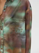 Camisa oversize de viscosa con estampado tipo tie-dye en tonos azulados. Presenta cuello clásico, cierre frontal con botones, bolsillo frontal con bordado y detalles de vivos en contraste en la tapeta y puños.