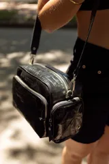 Bolso bandolera negro de cuero, con correa ajustable y desmontable. Tiene un compartimento principal con cierre y dos bolsillos frontales con cierre.