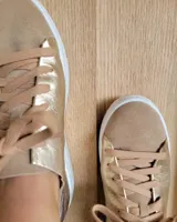 Zapatillas urbanas de cuero metalizado dorado y gamuza beige, con cordones anchos al tono y suela blanca.