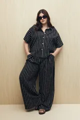 Conjunto de camisa y pantalón a rayas verticales en blanco y negro. La camisa es de manga corta, confeccionada en viscosa suave y fluida, con cuello clásico y botones al frente. El pantalón es de corte palazzo, con cintura alta y pernera ancha.