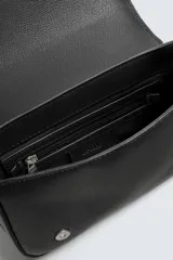 Bandolera negra con textura grabada, compartimento principal con cierre de solapa imantada, bolsillo interior con cremallera y asa de hombro ajustable.