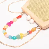 Cartera de mano con estructura rígida de madera clara, cuerpo de tejido de paja trenzado color verde claro y cierre de dos esferas blancas. Incluye un asa desmontable compuesta por cuentas irregulares de resina en tonos pastel y vibrantes.