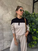 Sudadera con capucha de manga larga, color beige, con canesú negro en la parte superior de los hombros y capucha negra. Presenta cordones negros para ajustar la capucha.