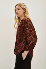 Camisa de manga larga con estampado animal print en tonos caramelo y negro. Presenta un escote en V con una solapa central en color negro y puños elásticos.